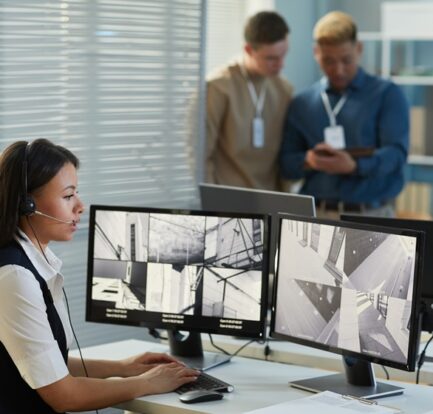 Side view portrait of young woman wearing headset while watching surveillance camera feed in security and monitoring office, copy space