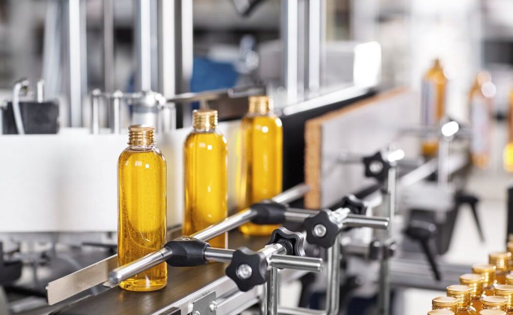 Clear bottles filled with yellow liquid move along an automated production line in a factory setting.