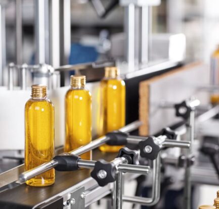 Clear bottles filled with yellow liquid move along an automated production line in a factory setting.